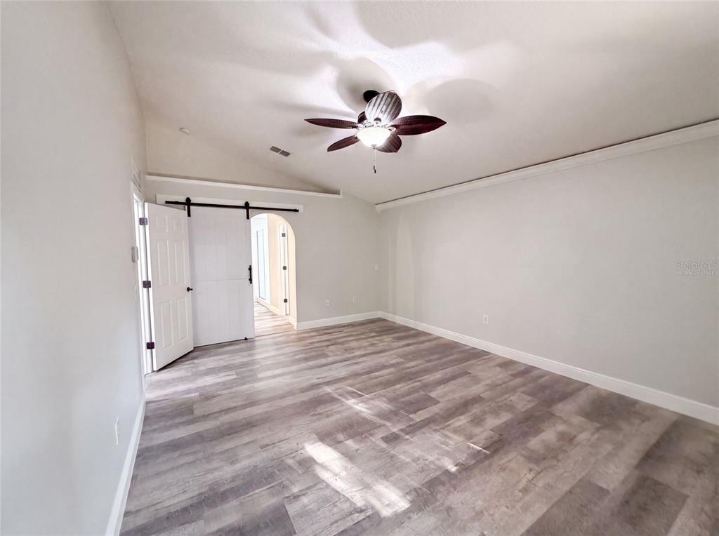 A room with light-colored walls, wood-look flooring, a vaulted ceiling, and a sliding barn door — 106 CABRILLO DRIVE, GROVELAND, FL