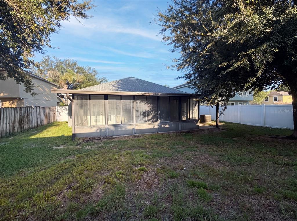 A backyard view of a house featuring a large screened-in porch and a white fence — 106 CABRILLO DRIVE, GROVELAND, FL