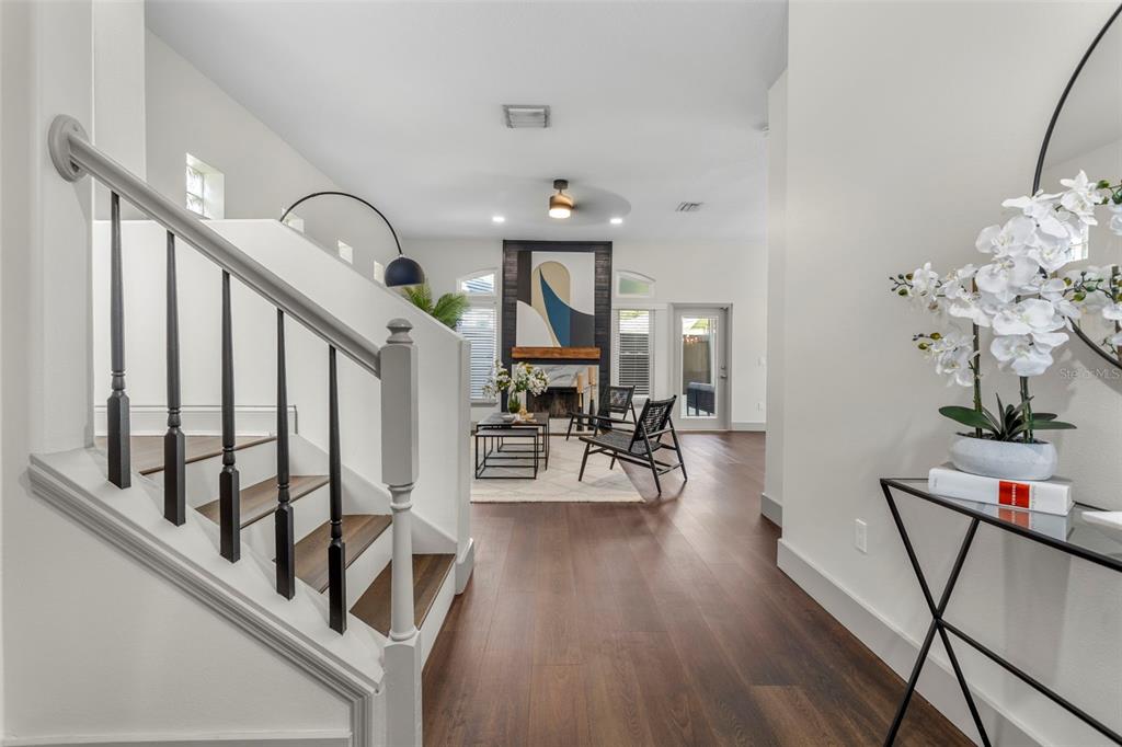 A staircase with black railings leads toward a living room featuring a fireplace and windows — 7032 SOMERTON BOULEVARD UNIT 54, ORLANDO, FL