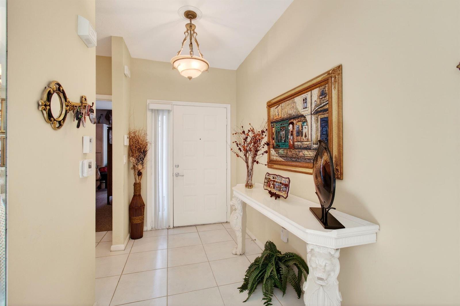 A bright entryway features a white front door, tiled floors, and a decorative console table — 12527 Crystal Pointe Drive # C, Boynton Beach FL 33437, BOYNTON BEACH, FL