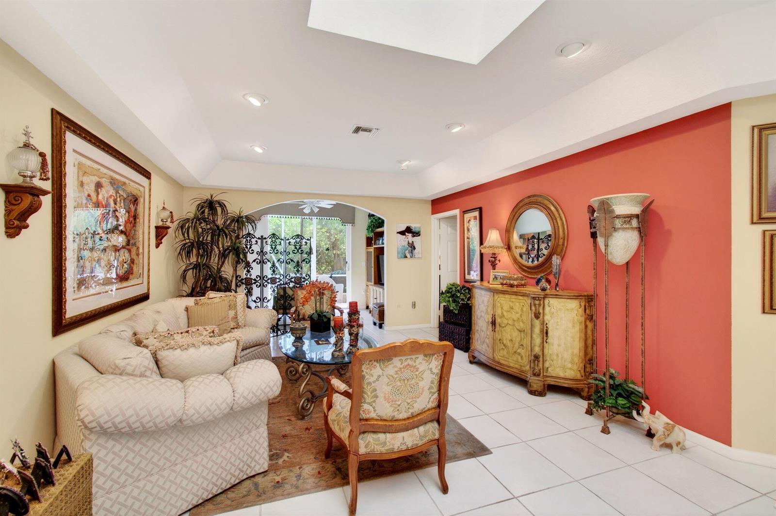 A living room features a coral accent wall, tiled floors, and a tray ceiling — 12527 Crystal Pointe Drive # C, Boynton Beach FL 33437, BOYNTON BEACH, FL