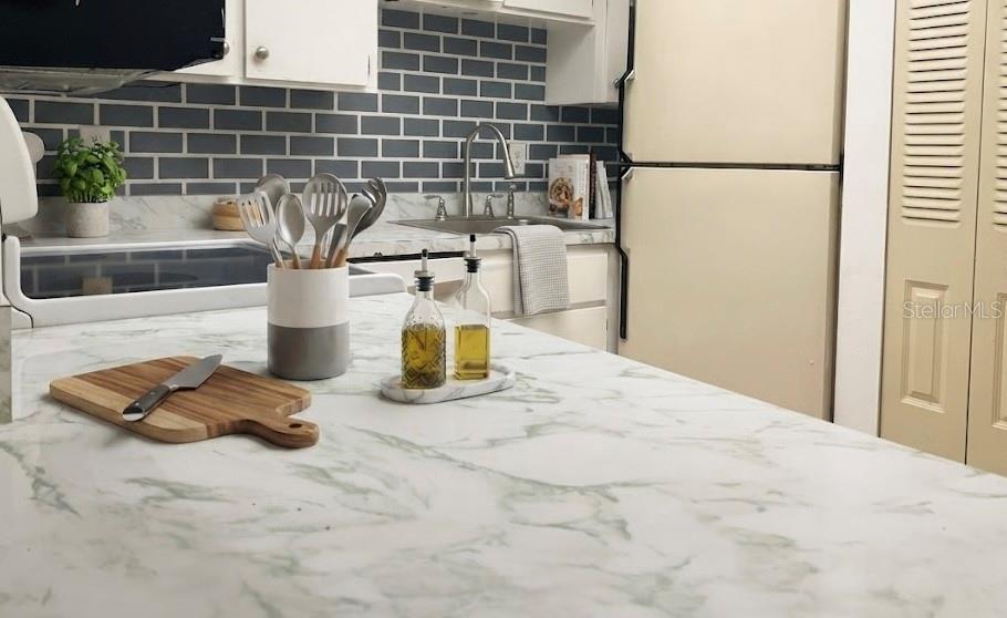 A kitchen features a marble-patterned island, white cabinets, and a gray subway tile backsplash — 729 MIDWAY DRIVE UNIT B, OCALA, FL