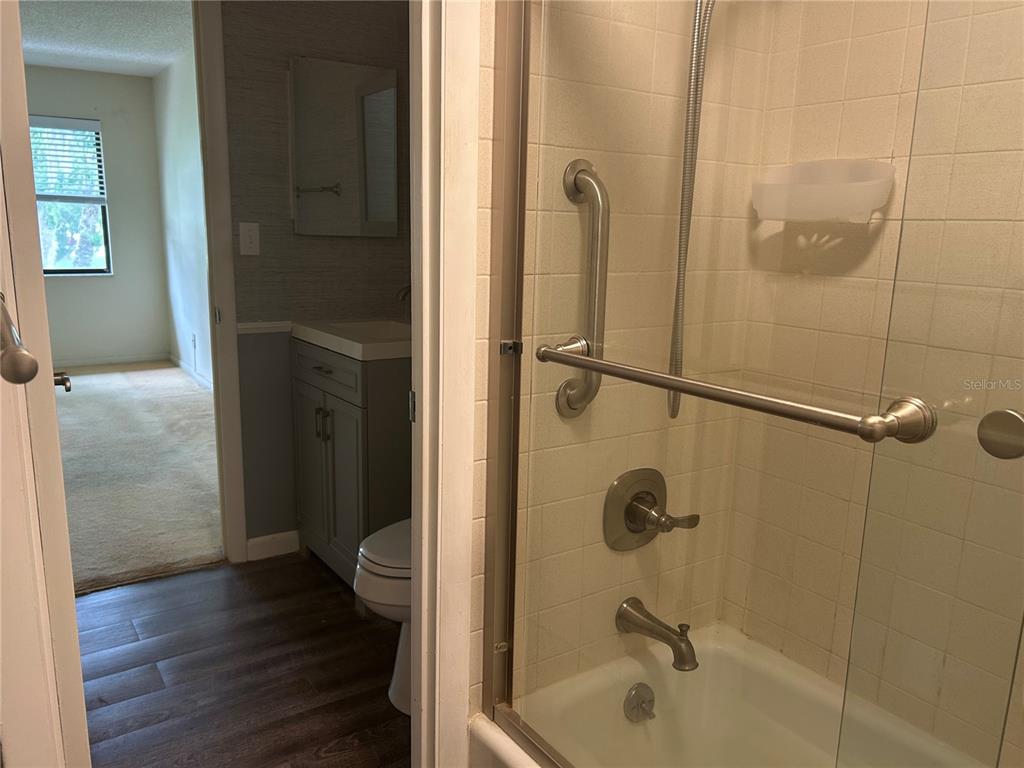 A bathroom features a glass-enclosed shower with grab bars next to a vanity and toilet — 729 MIDWAY DRIVE UNIT B, OCALA, FL