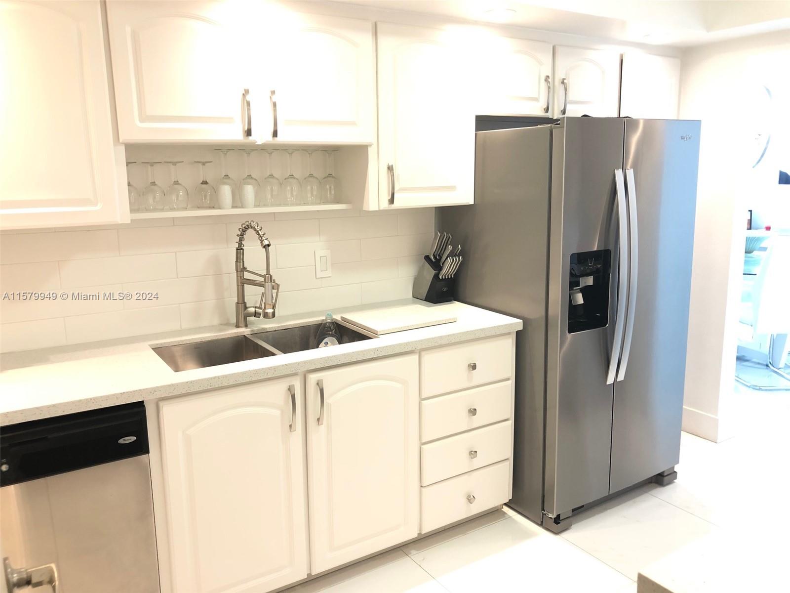 A kitchen features white cabinets, stainless steel appliances, a double sink, and a tiled backsplash — 3901 S Ocean Dr # 14M, Hollywood FL 33019, HOLLYWOOD, FL
