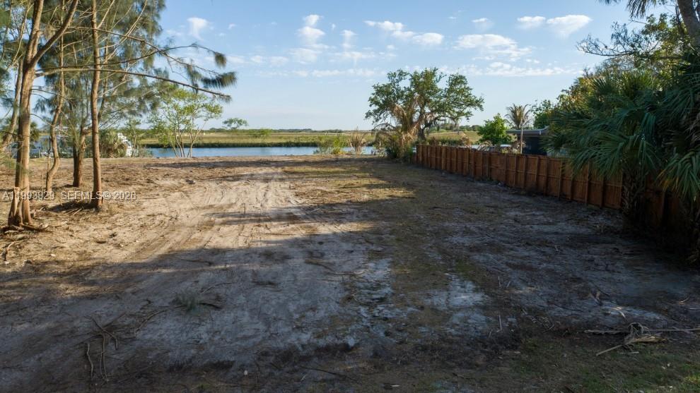 A vacant, sandy lot features a wooden fence and trees overlooking a body of water — 1035 W Anchor Lane, Moore Haven FL 33471, MOORE HAVEN, FL