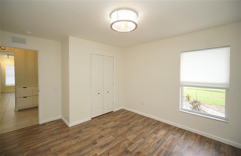 An empty bedroom features wood-look flooring, a white closet, a window, and a ceiling light — 5225 ALGERINE PLACE, WESLEY CHAPEL, FL