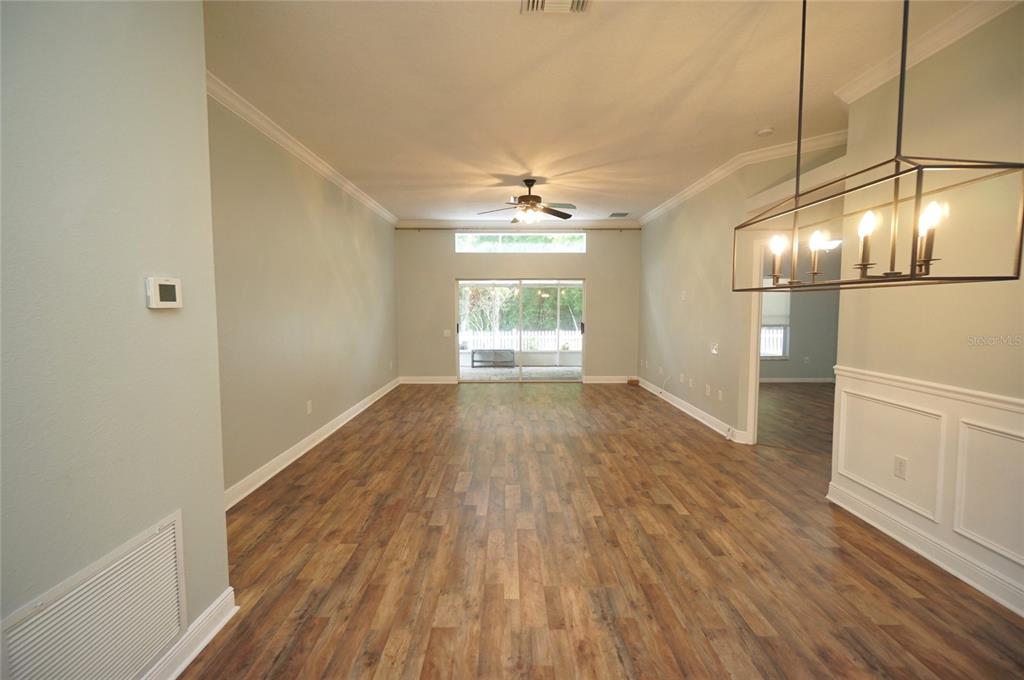 An open living area features wood-look flooring, a ceiling fan, and a sliding glass door — 5225 ALGERINE PLACE, WESLEY CHAPEL, FL