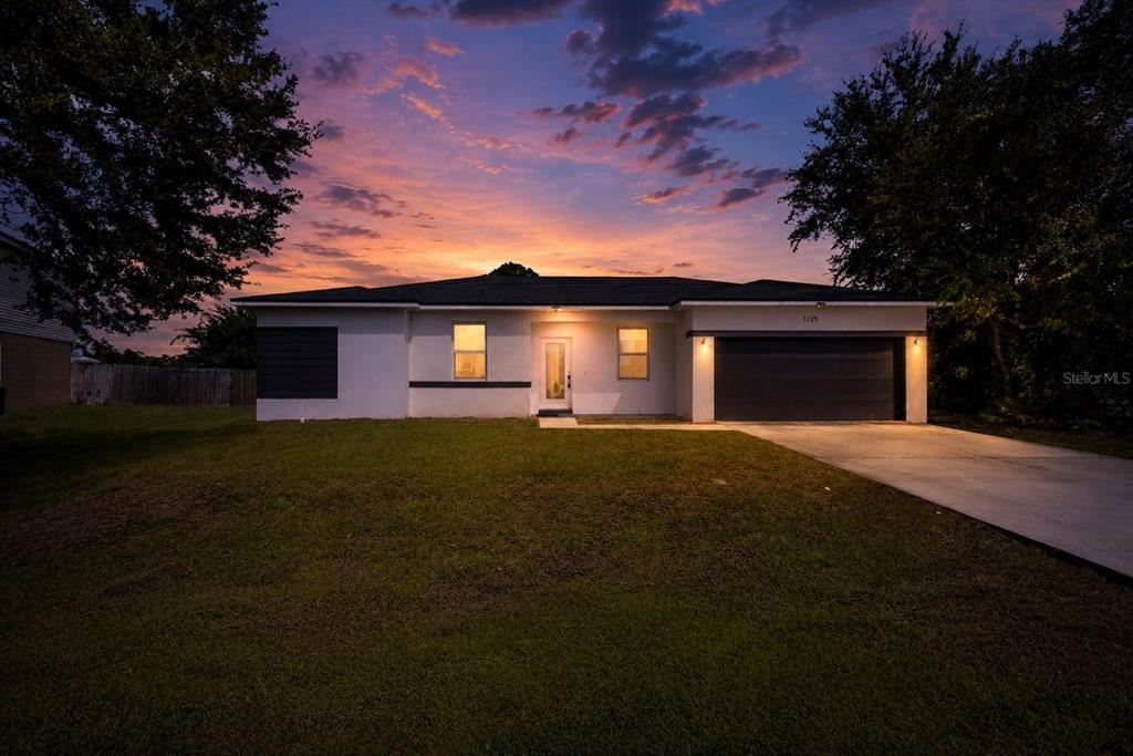 A single-story house with a dark garage door and white exterior at sunset — 1125 MUNSTER COURT, KISSIMMEE, FL