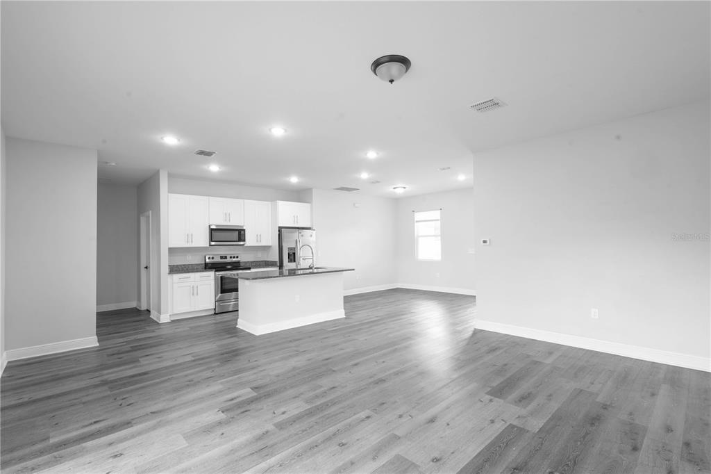 An open-concept kitchen and living area featuring white cabinets, stainless appliances, and gray flooring — 1125 MUNSTER COURT, KISSIMMEE, FL