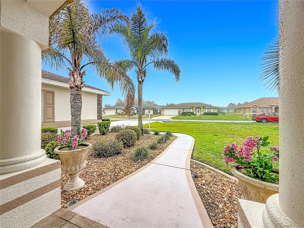 A concrete walkway leads through a landscaped front yard with palm trees and potted flowers — 5028 NW 34TH PLACE, OCALA, FL