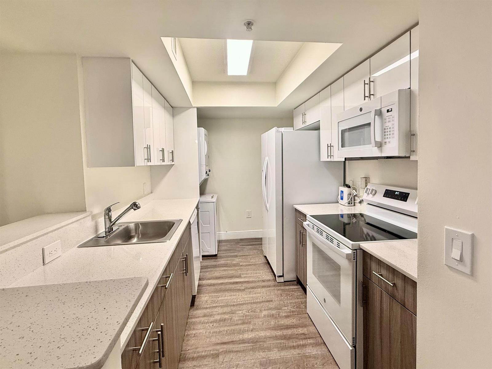 A galley kitchen features white upper cabinets, wood-tone lower cabinets, quartz countertops, and white appliances — 18335 NW 68 Avenue # 406, Hialeah FL 33015, HIALEAH, FL