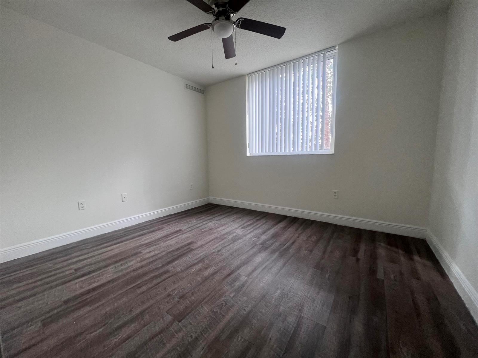 An empty bedroom features white walls, dark wood-look flooring, a ceiling fan, and vertical blinds — 18335 NW 68 Avenue # 406, Hialeah FL 33015, HIALEAH, FL