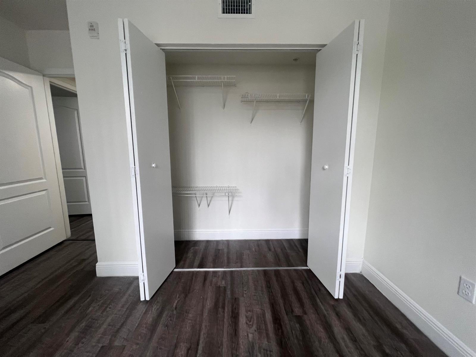An open closet with white wire shelving against a light wall and dark wood flooring — 18335 NW 68 Avenue # 406, Hialeah FL 33015, HIALEAH, FL