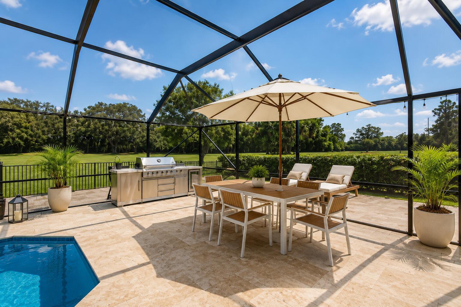 A covered patio with a swimming pool, outdoor kitchen, dining set, and umbrella overlooking greenery — 10710 Boca Woods Lane, Boca Raton FL 33428, BOCA RATON, FL