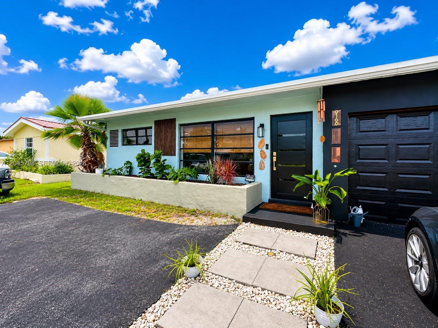 A light blue house exterior features a black front door, garage, and a stone planter — 9160 NW 26th Pl, Sunrise FL 33322, SUNRISE, FL