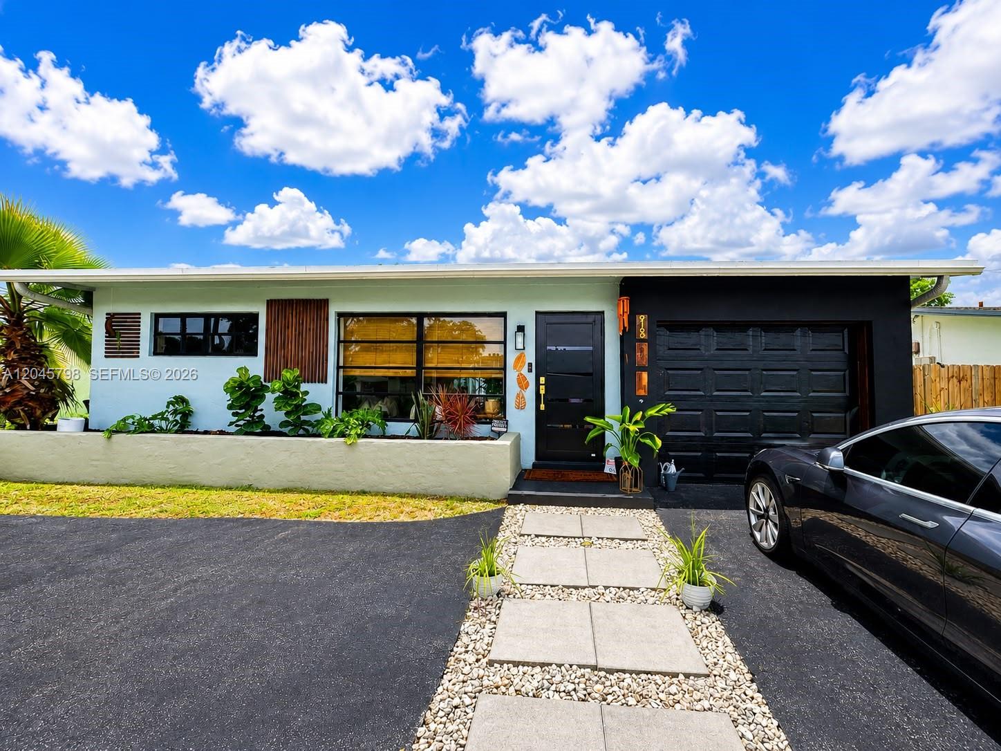 A single-story house features a light blue facade, black garage door, and a stone walkway — 9160 NW 26th Pl, Sunrise FL 33322, SUNRISE, FL