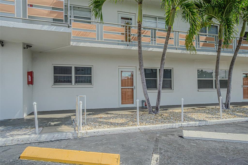 A ground-level apartment entrance features a glass storm door, white walls, and palm trees — 3128 59TH STREET S UNIT 110, GULFPORT, FL