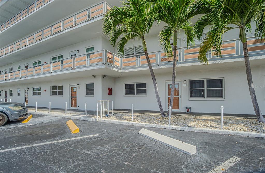 A two-story apartment building exterior features a parking lot, palm trees, and balcony railings — 3128 59TH STREET S UNIT 110, GULFPORT, FL