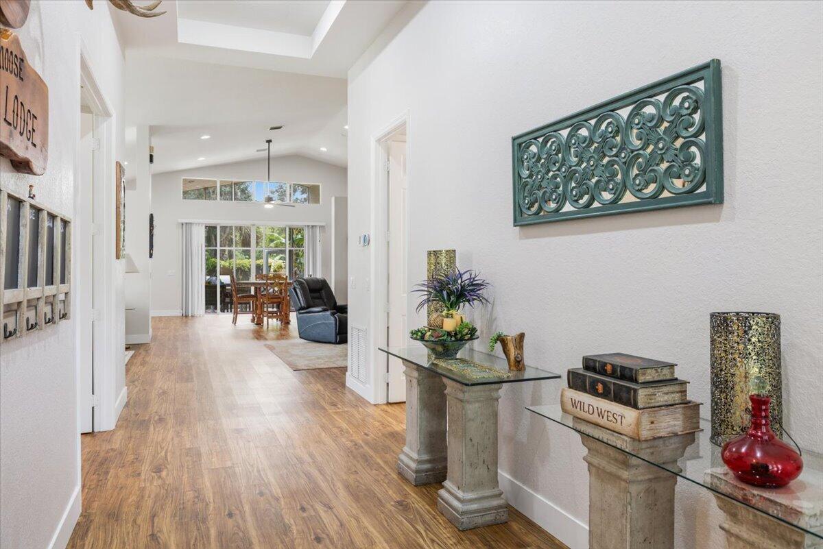 A hallway with wood-look flooring leads to a dining area with large windows — 5185 Topaz Lane SW, Vero Beach FL 32968, VERO BEACH, FL