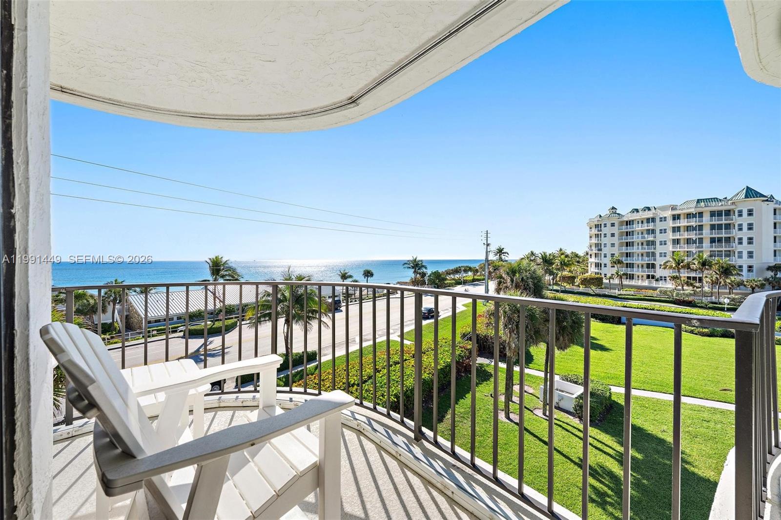 A balcony with a white chair overlooks a road, green lawn, and the ocean — 1300 S Highway A1a # 402, Jupiter FL 33477, JUPITER, FL