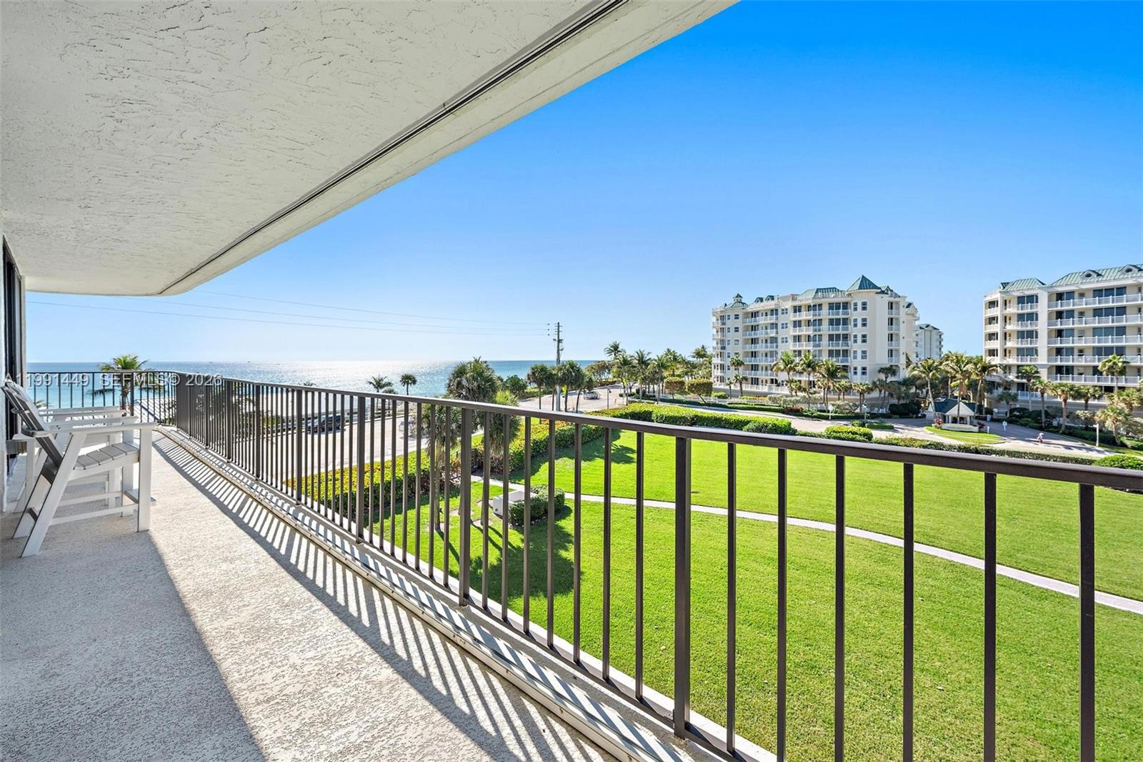 A balcony with a metal railing overlooks a grassy lawn, palm trees, and the ocean — 1300 S Highway A1a # 402, Jupiter FL 33477, JUPITER, FL