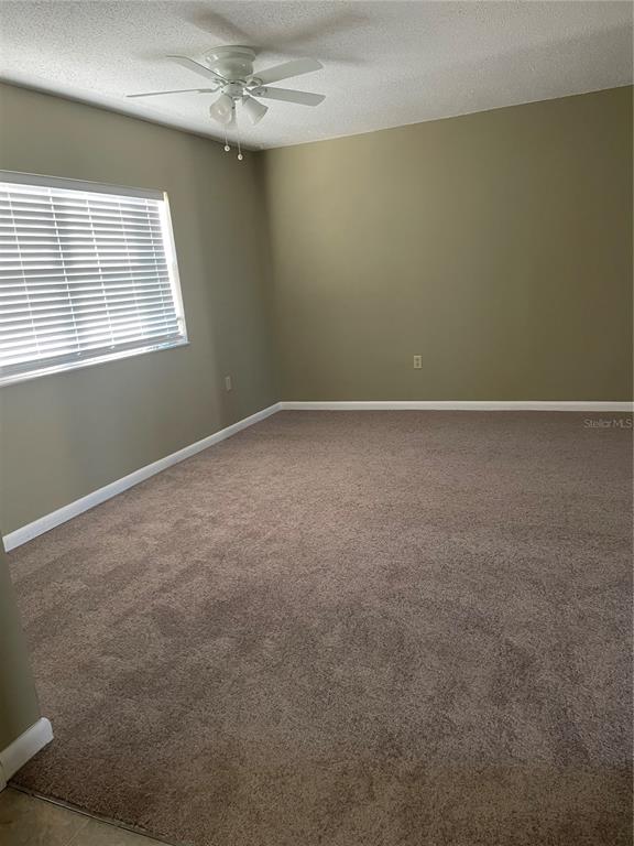 An empty bedroom features beige walls, brown carpeting, a ceiling fan, and a window with blinds — 7701 STARKEY ROAD UNIT 622, SEMINOLE, FL