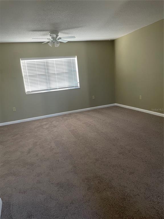 An empty room features beige walls, brown carpeting, a ceiling fan, and a window — 7701 STARKEY ROAD UNIT 622, SEMINOLE, FL