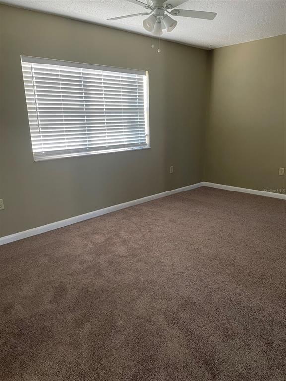 An empty bedroom features beige walls, brown carpeting, a ceiling fan, and a window with blinds — 7701 STARKEY ROAD UNIT 622, SEMINOLE, FL