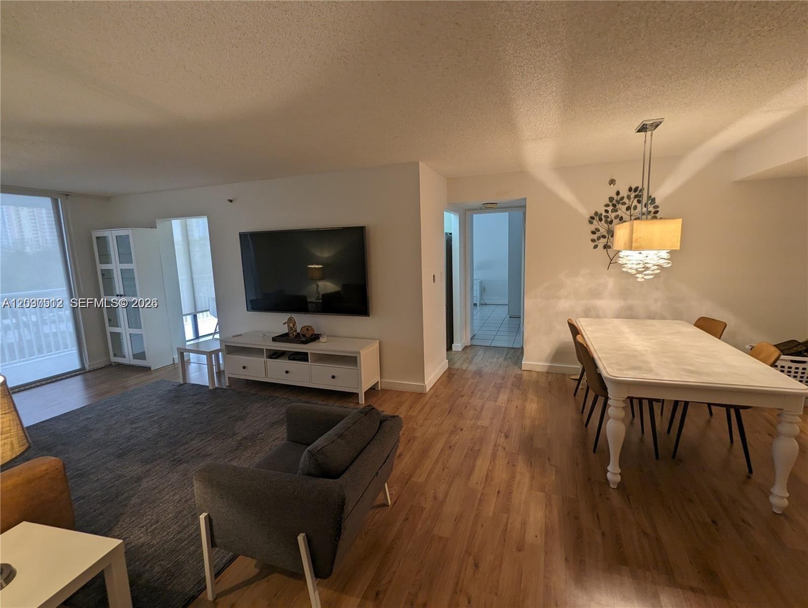 A living and dining area features wood-look flooring, a wall-mounted television, and a chandelier — SUNNY ISLES BEACH, FL