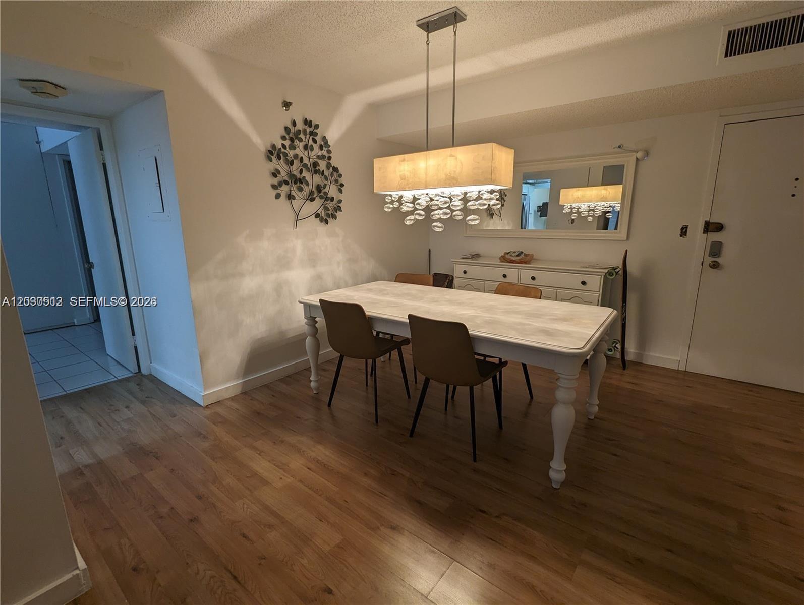 A dining room features a white table, four chairs, a chandelier, and wood flooring — SUNNY ISLES BEACH, FL