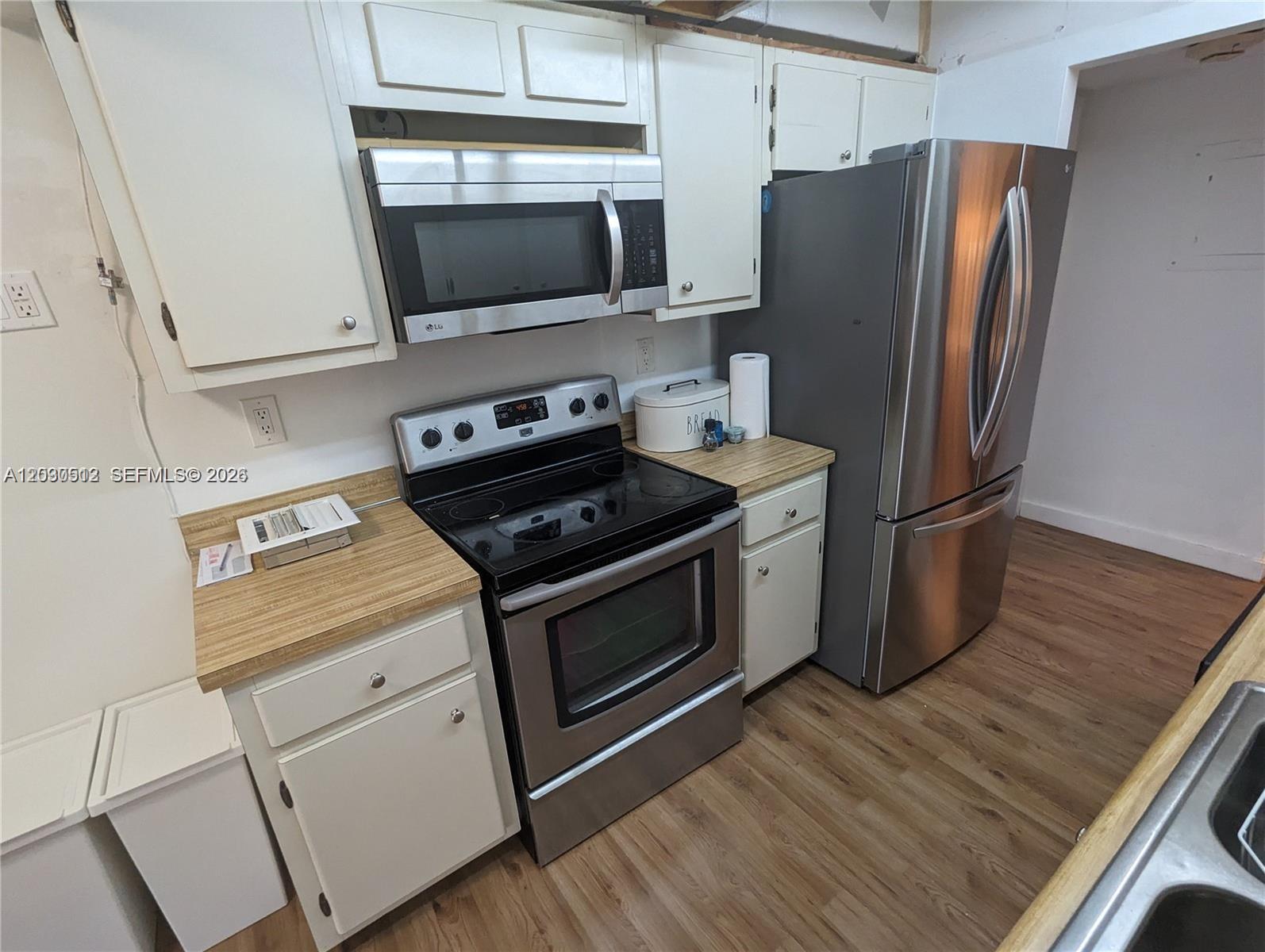 A kitchen features white cabinets, stainless steel appliances, and wood-look flooring — SUNNY ISLES BEACH, FL