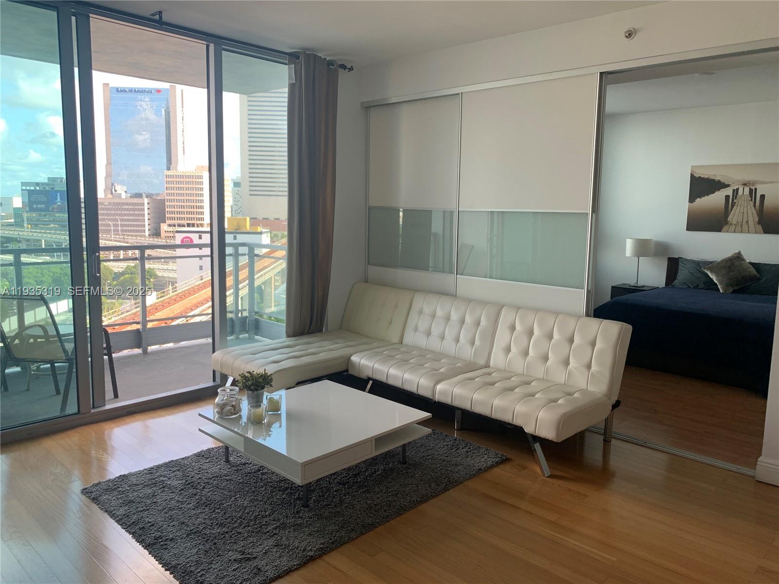 A living room features a white tufted sofa, a coffee table, and a balcony view — 90 SW 3rd St # 1211, Miami FL 33130, MIAMI, FL