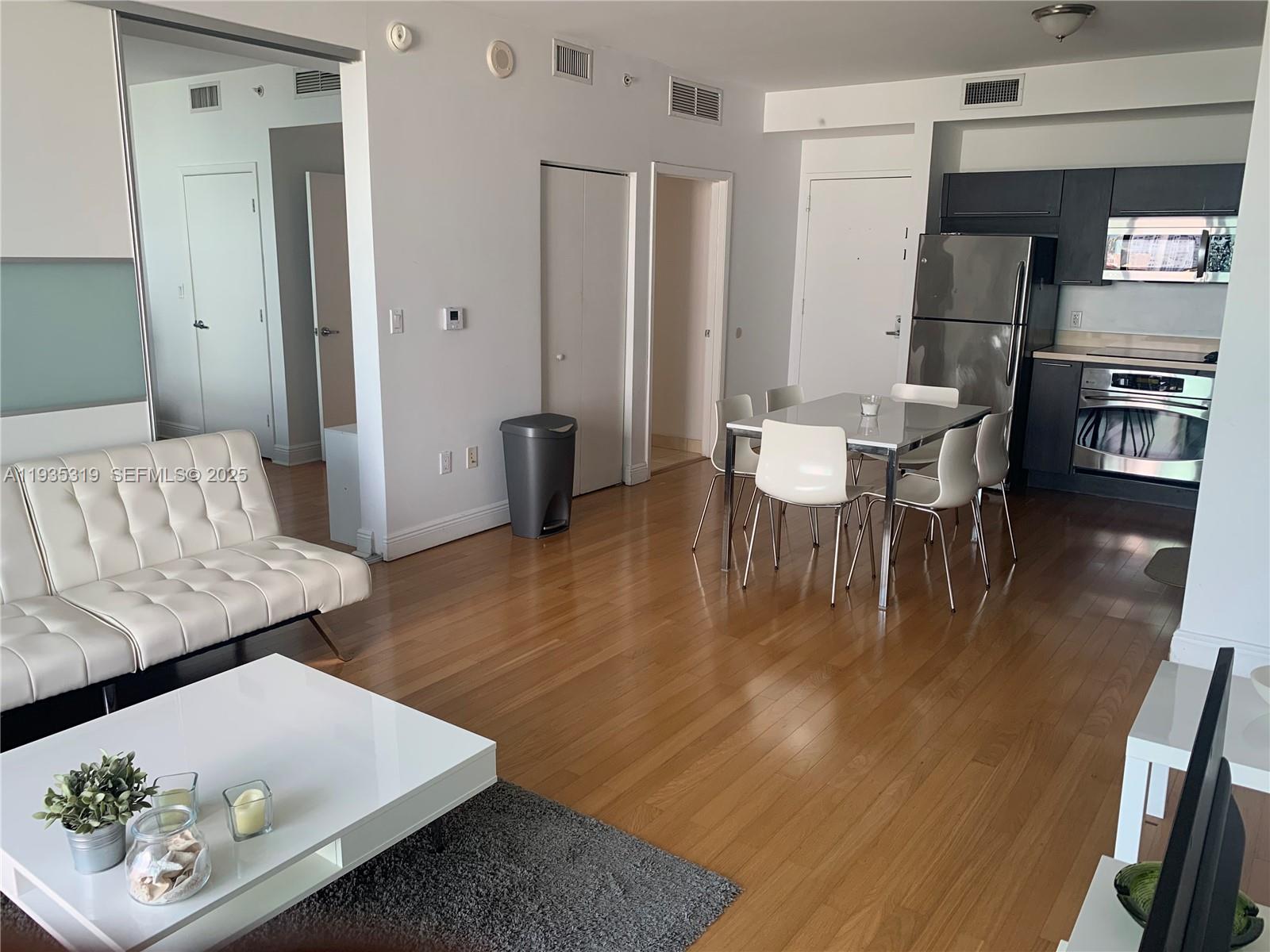 An open-concept living and dining area features hardwood floors, white furniture, and a modern kitchen — 90 SW 3rd St # 1211, Miami FL 33130, MIAMI, FL