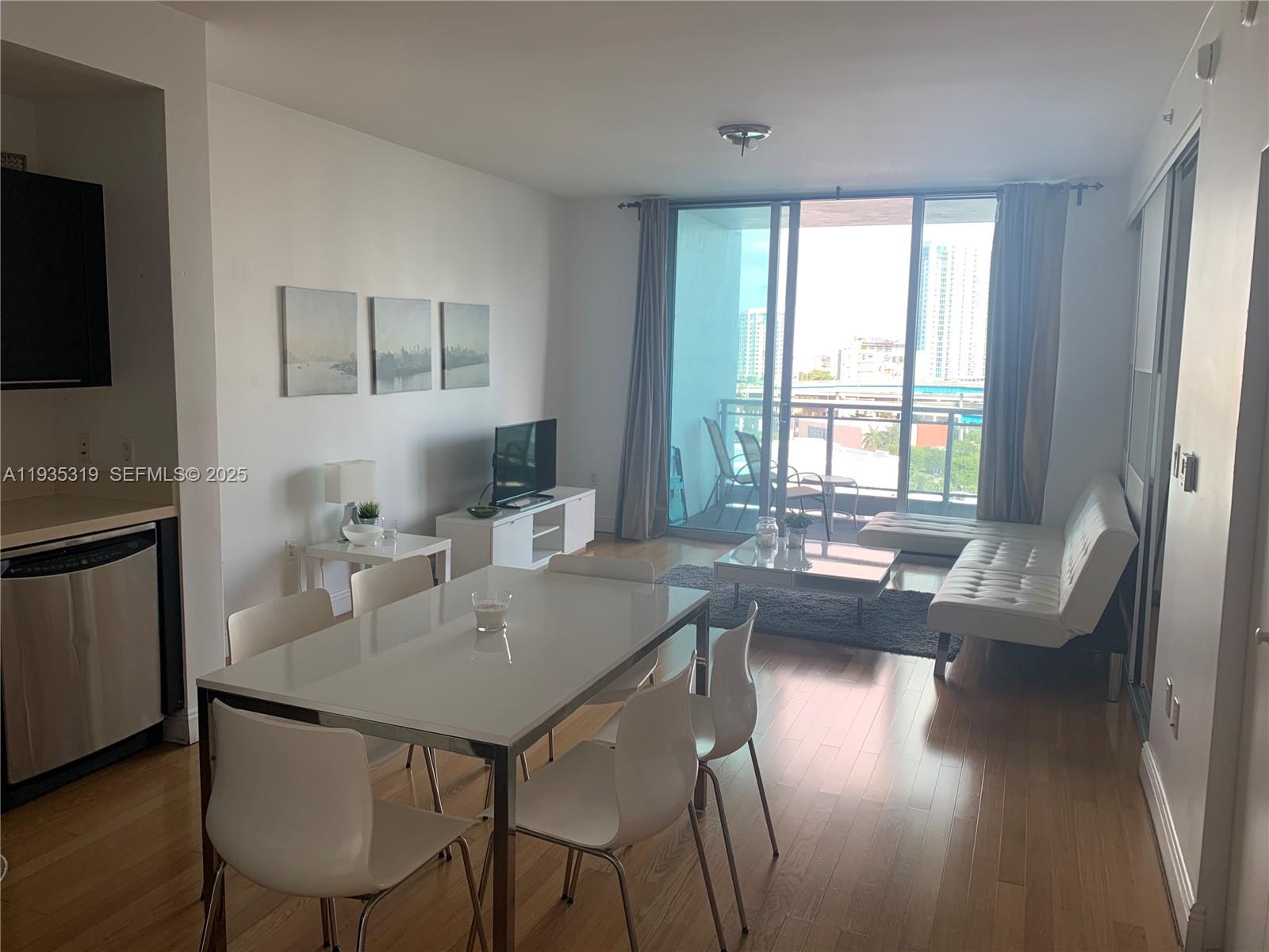 A bright living and dining area features white furniture, hardwood floors, and a balcony view — 90 SW 3rd St # 1211, Miami FL 33130, MIAMI, FL