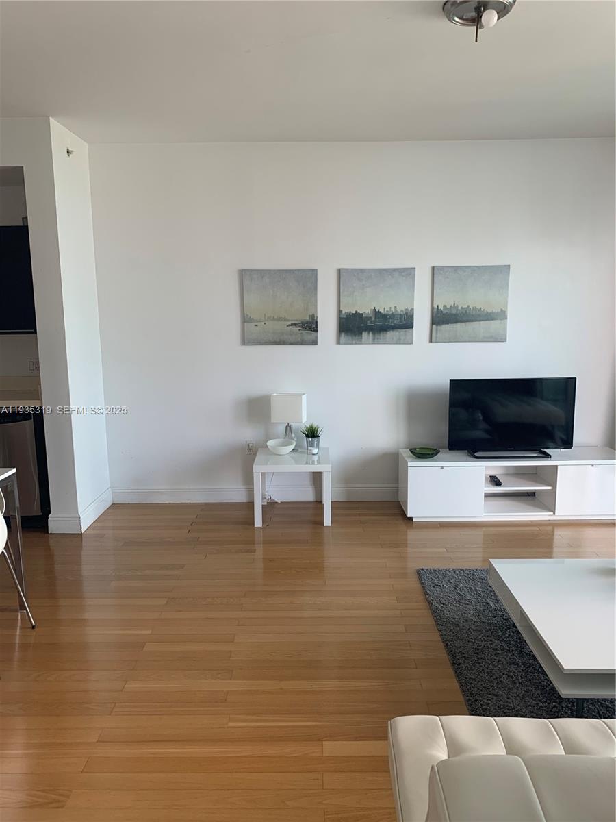 A living room features light wood floors, white furniture, and three landscape paintings on the wall — 90 SW 3rd St # 1211, Miami FL 33130, MIAMI, FL