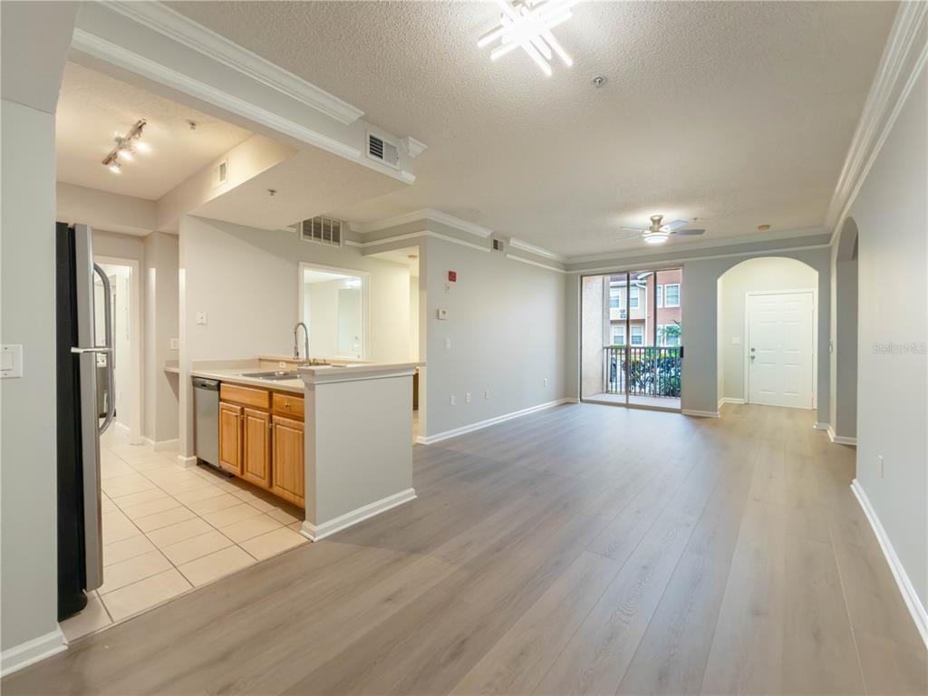 An open-concept living area features light wood-look flooring, a kitchen with wooden cabinets, and a balcony — 12203 WILD IRIS WAY UNIT 108, ORLANDO, FL