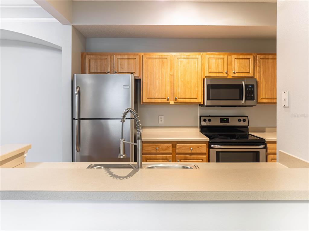 A kitchen features light wood cabinets, stainless steel appliances, and a beige countertop — 12203 WILD IRIS WAY UNIT 108, ORLANDO, FL
