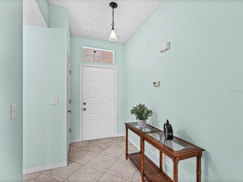 An entryway features light blue walls, tile flooring, a glass-topped console table, and a pendant light — 830 MCCALLISTER AVENUE, SUN CITY CENTER, FL