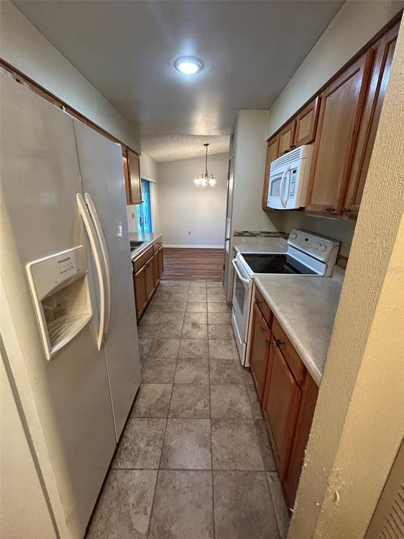 A galley kitchen features wood cabinets, a white refrigerator, and tile flooring — 955 N SUNSET DRIVE, MOUNT DORA, FL