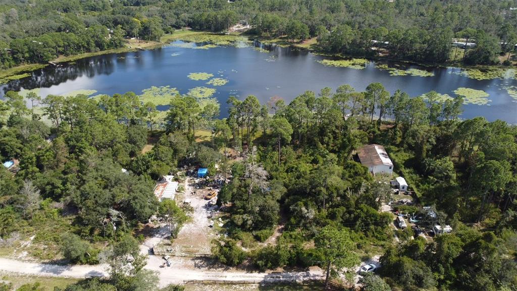 An aerial view shows a wooded property with a lake, two buildings, and a dirt road — 42318 W LAKE ROAD, DELAND, FL