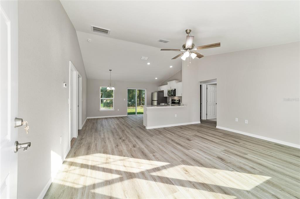 An open-concept living area with light wood-look flooring, vaulted ceilings, and a kitchen island — 44 ALMOND ROAD, OCALA, FL
