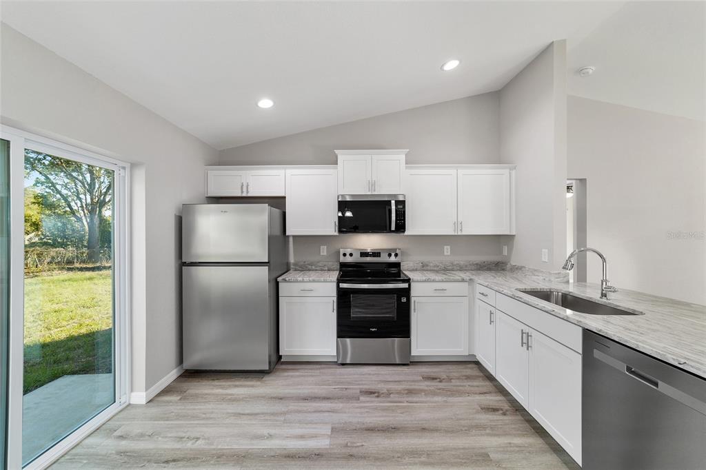 A modern kitchen features white cabinets, stainless steel appliances, marble-look countertops, and wood-look flooring — 44 ALMOND ROAD, OCALA, FL