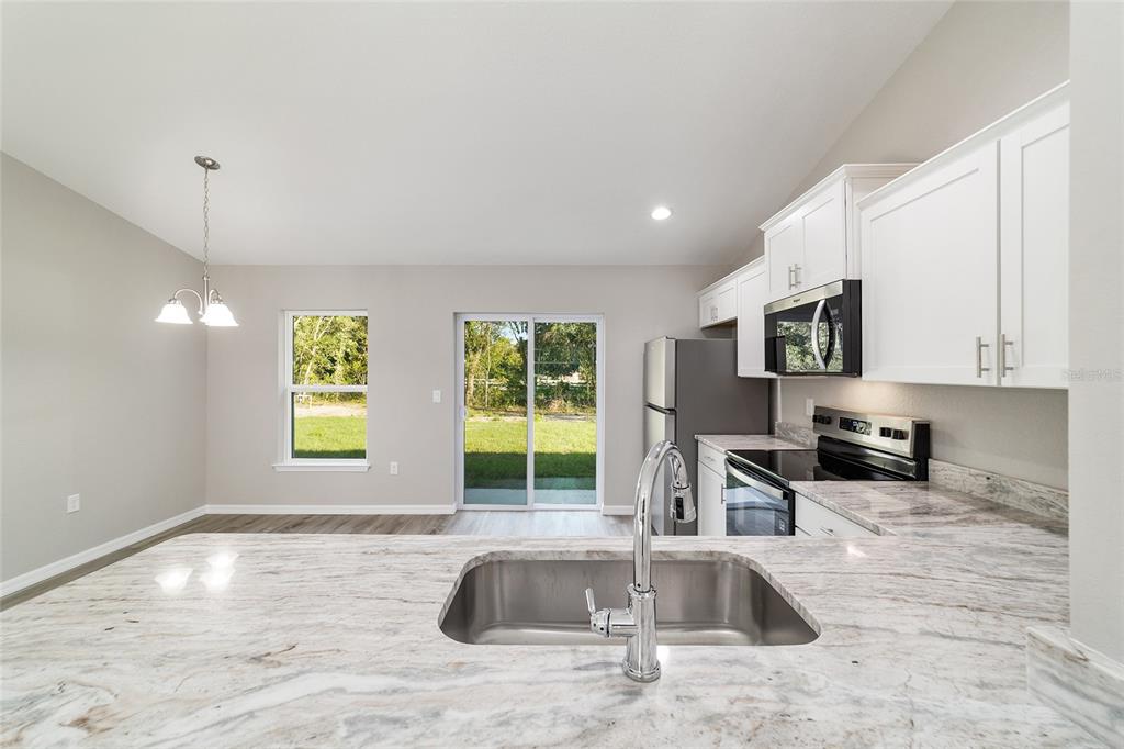 A kitchen with white cabinets, granite countertops, and a stainless steel sink overlooks a dining area — 44 ALMOND ROAD, OCALA, FL