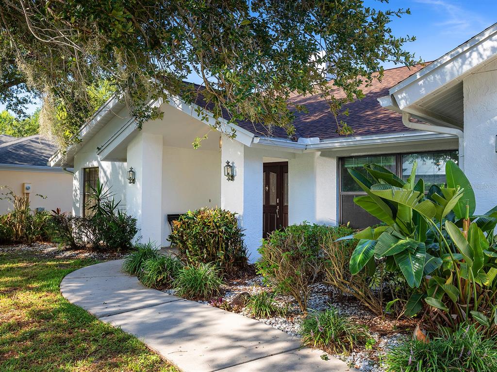 A white house with a covered entryway, a concrete walkway, and lush landscaping — 1756 COTTONWOOD TRAIL, SARASOTA, FL