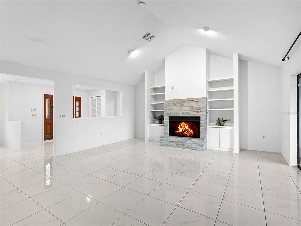 A bright living room features white tile floors, a stone fireplace, and built-in shelving — 1756 COTTONWOOD TRAIL, SARASOTA, FL