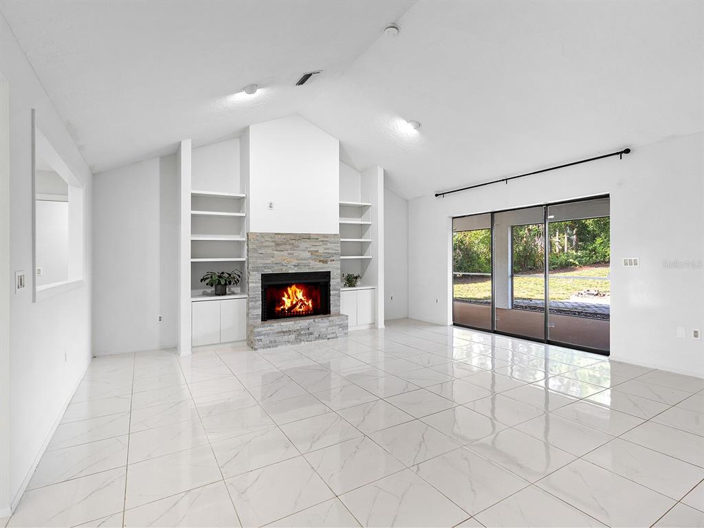 A living room features white tile floors, a stone fireplace, built-in shelves, and sliding glass doors — 1756 COTTONWOOD TRAIL, SARASOTA, FL
