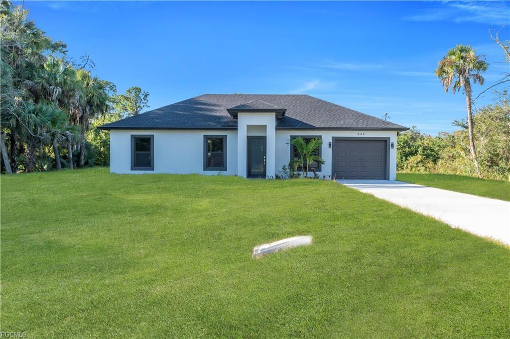 A single-story house with a white exterior, dark roof, and attached garage sits on grass — 644 WOODCREST DR, LEHIGH ACRES, FL