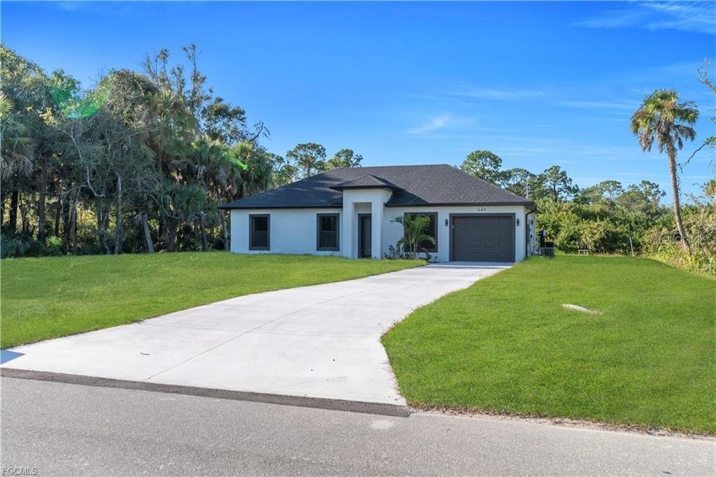 A single-story house with a white exterior, dark roof, and a concrete driveway — 644 WOODCREST DR, LEHIGH ACRES, FL