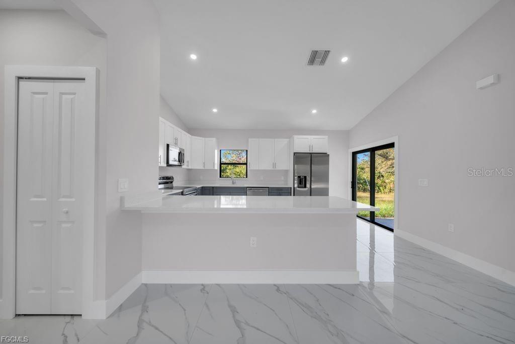 A modern kitchen features white cabinetry, a breakfast bar, and light-colored marble-patterned tile flooring — 644 WOODCREST DR, LEHIGH ACRES, FL