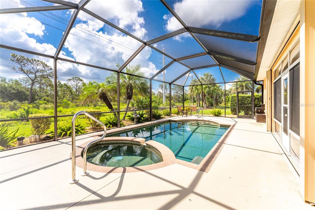 A screened-in lanai features a swimming pool, an attached spa, and a view of trees — 682 BARNACLE COURT, ENGLEWOOD, FL